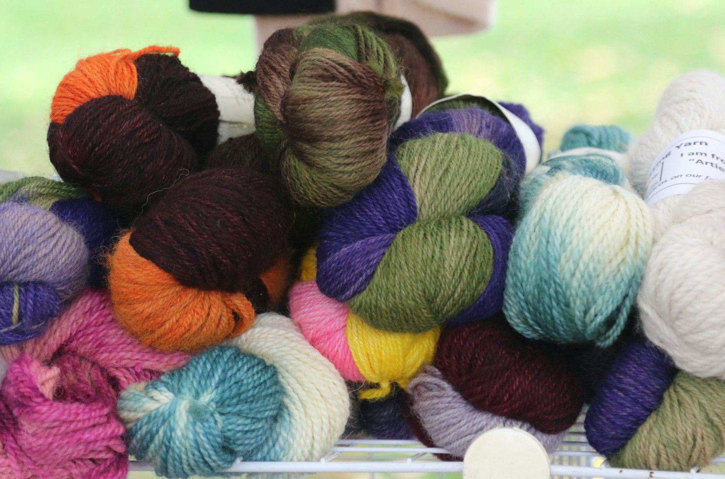 Diverse wool yarn skeins piled on a white wire shelf.