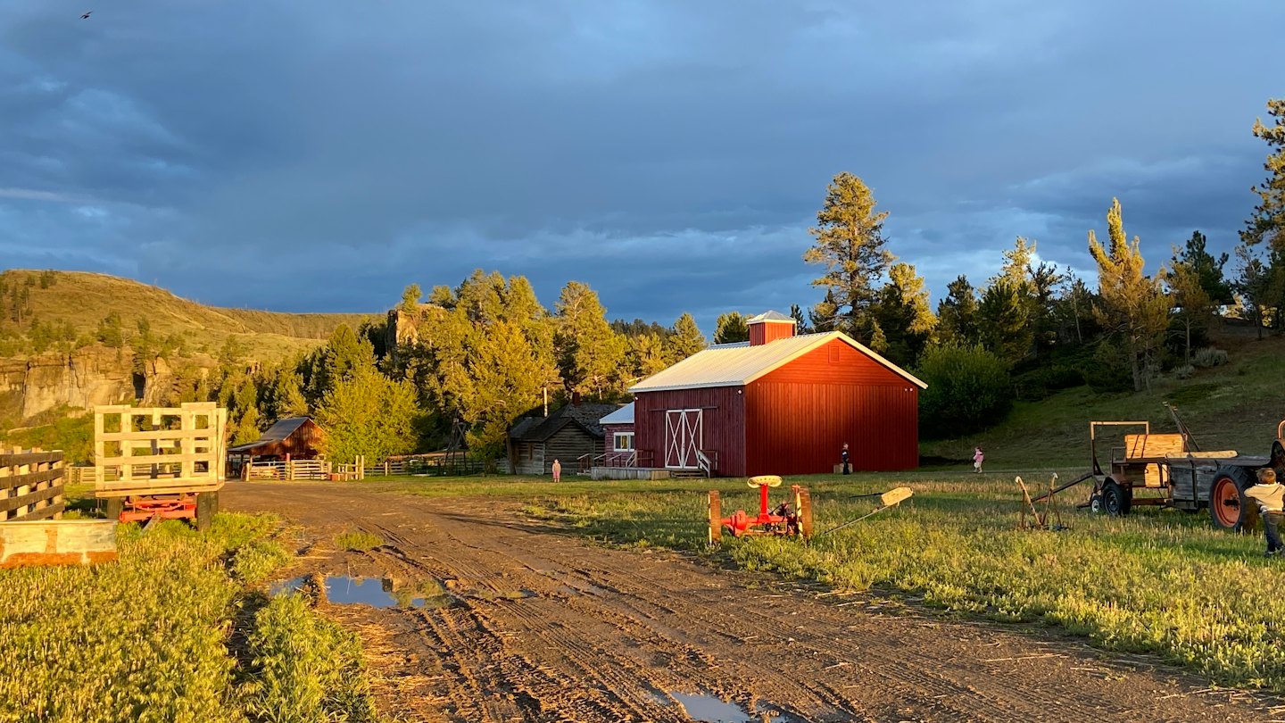 A red barn sits on a grassy hillside near evergreen trees.